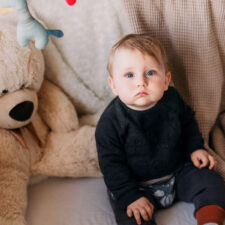 Kleinkind sitzt ernst zwischen Teddybären und schaut in die Kamera beim Familienshooting mit Natalia Schuchardt