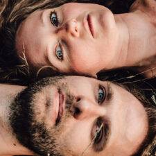 Pärchen liegt im Gras und schaut von unten in die Kamera beim Paarshooting München mit Natalia Schuchardt